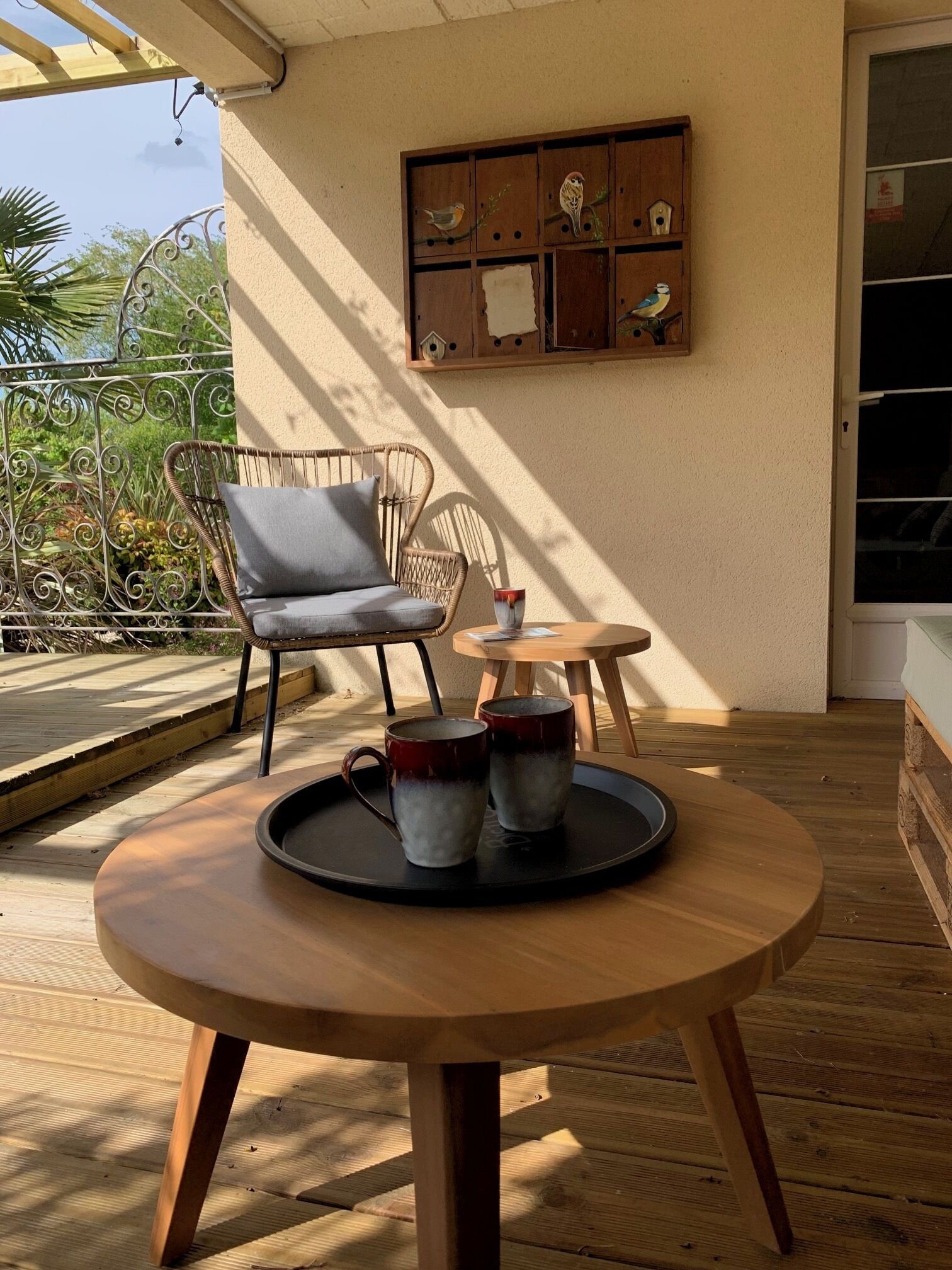 A wooden table with a tray holding two mugs, a wicker chair, a small round table, and a wall-mounted birdhouse display.