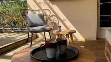 A wooden table with a tray holding two mugs, a wicker chair, a small round table, and a wall-mounted birdhouse display.