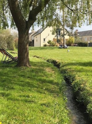 A grassy area with a tree, a small stream, and a building in the background. - "Les Nichoirs" Cozy cottage in Ussy in the Normandy countryside (Ussy)
