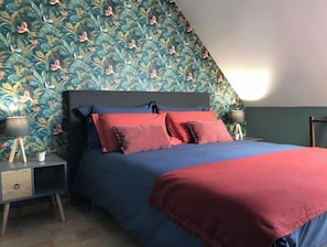 A bedroom with a bed, two bedside tables, and a wall with a floral pattern. - "Les Nichoirs" Cozy cottage in Ussy in the Normandy countryside (Ussy)
