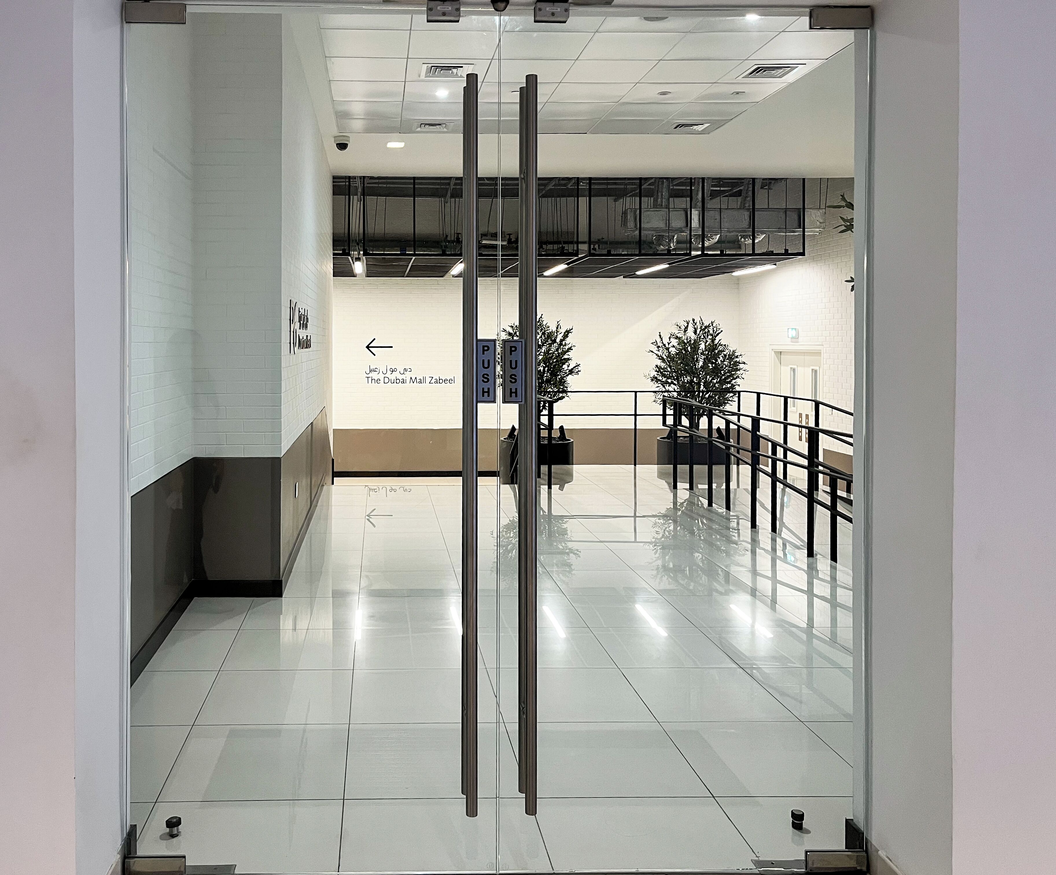 A modern interior with a glass door, a directional sign, and a potted plant.