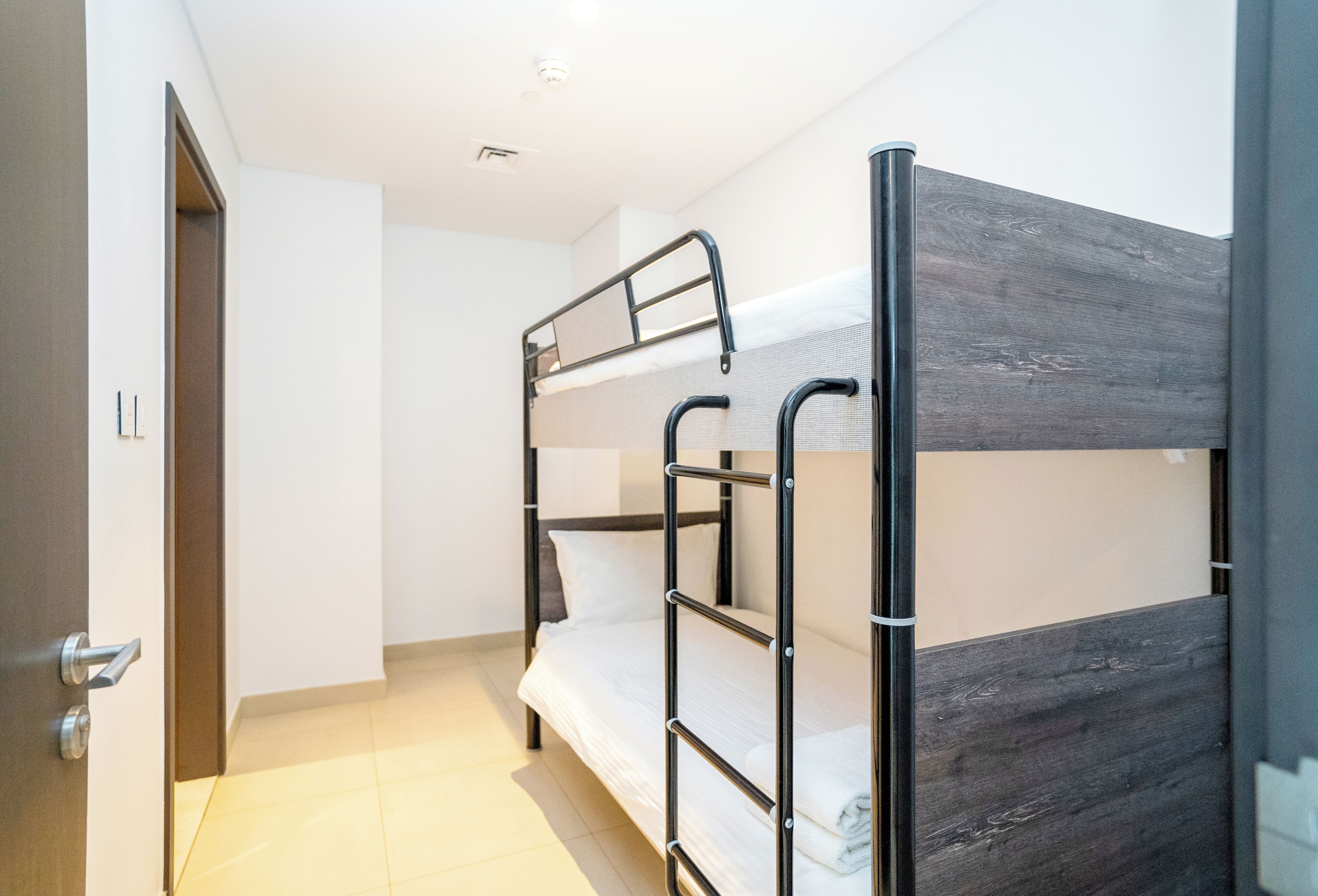 Quarto com beliche, cabeceira de madeira, porta com puxador prateado e piso de azulejos.
