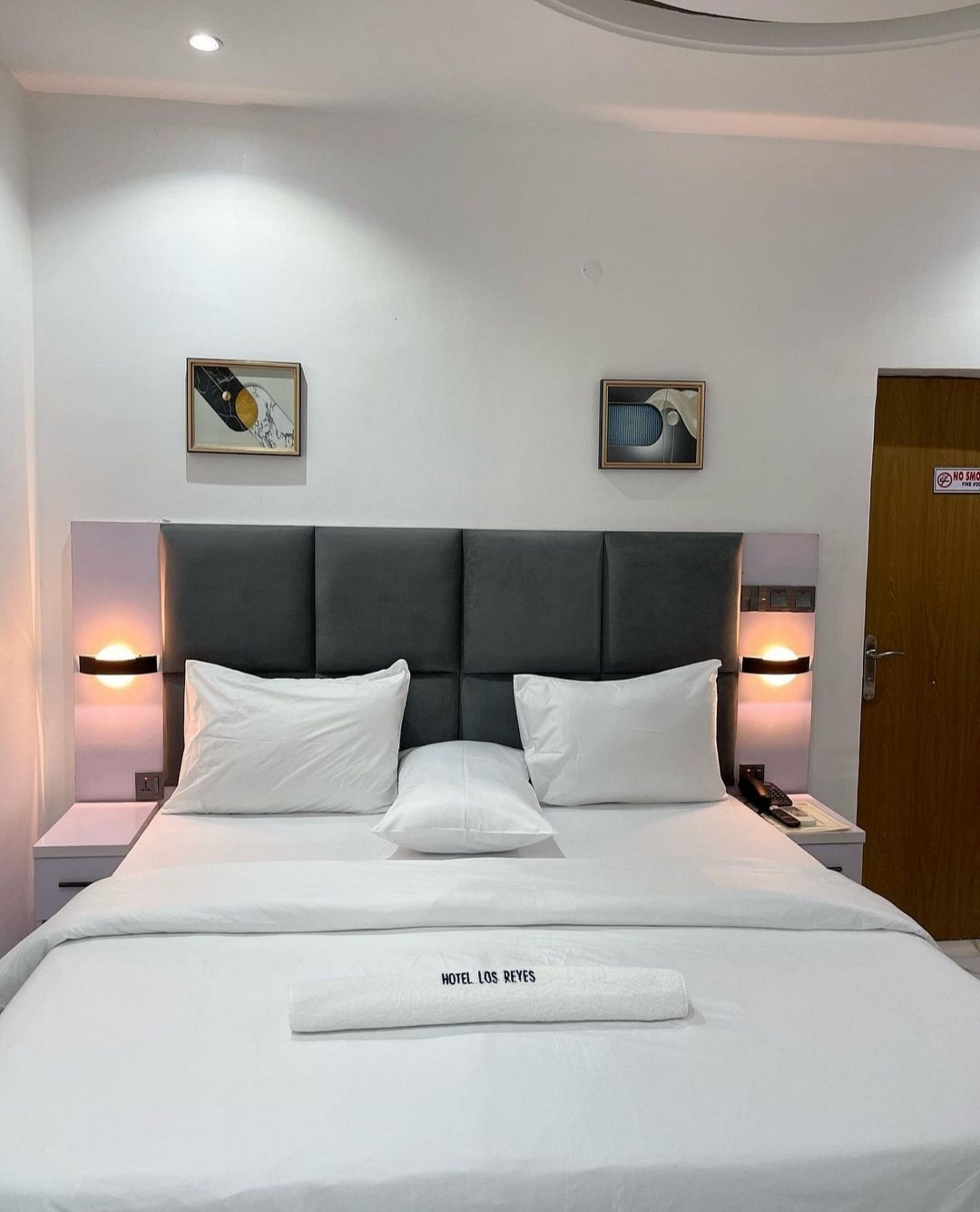 A neatly made bed with a headboard, two bedside tables with lamps, and two framed pictures on the wall.