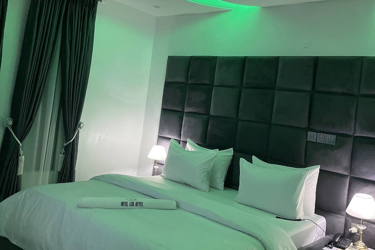 Een hotelkamer met een bed, nachtkastje, hoofdbord en een plafondlamp met gebogen kap.