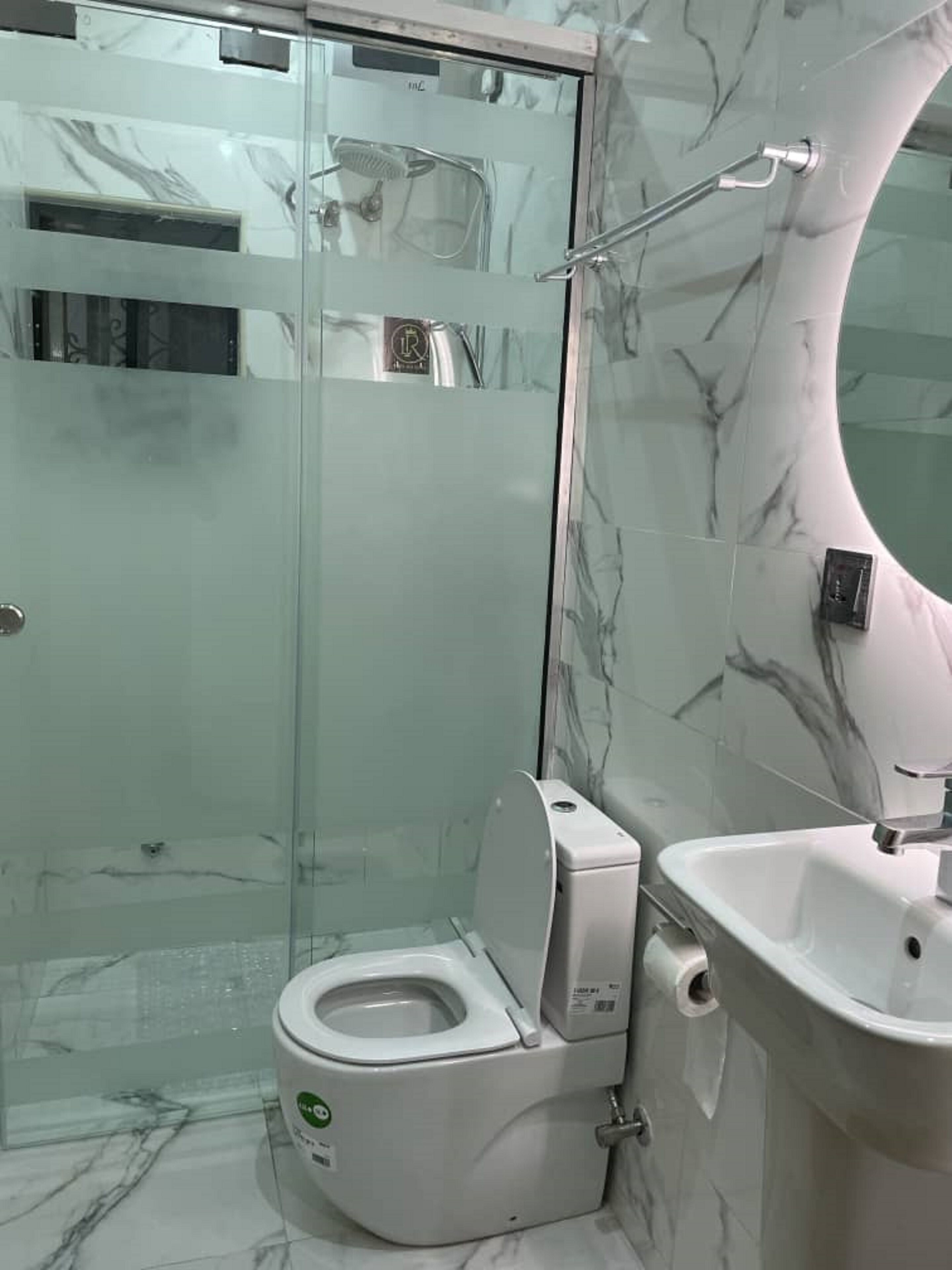 A modern bathroom with a glass-enclosed shower, a white toilet, and a sink with a marble backsplash.