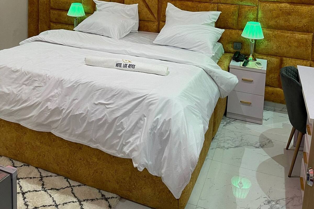 Een hotelkamer met een groot bed, twee nachtkastjes, een bureau en een hoofdbord met een geometrisch patroon.