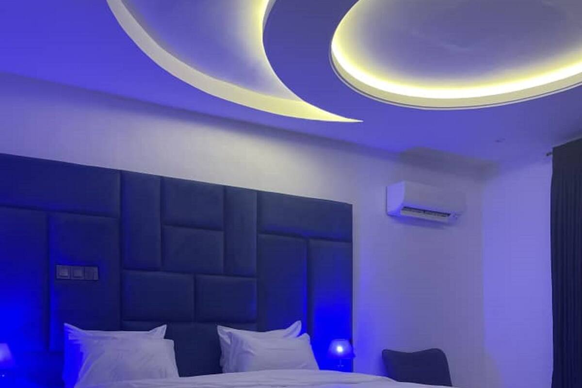 Een moderne slaapkamer met een donker hoofdbord, een groot bed en blauwe sfeerverlichting.