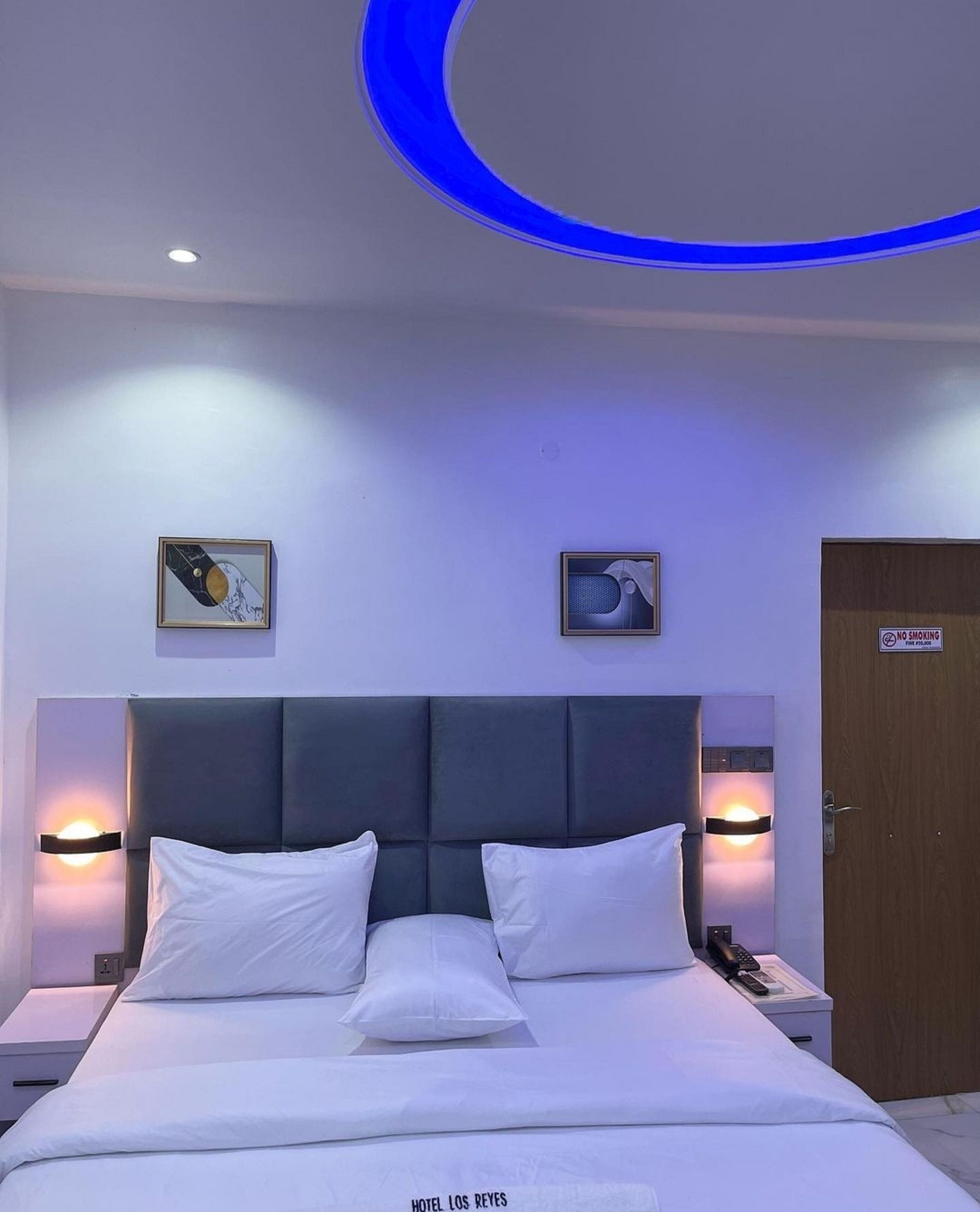 Une chambre d’hôtel moderne avec un grand lit, deux lampes fixées au mur et un luminaire au plafond.