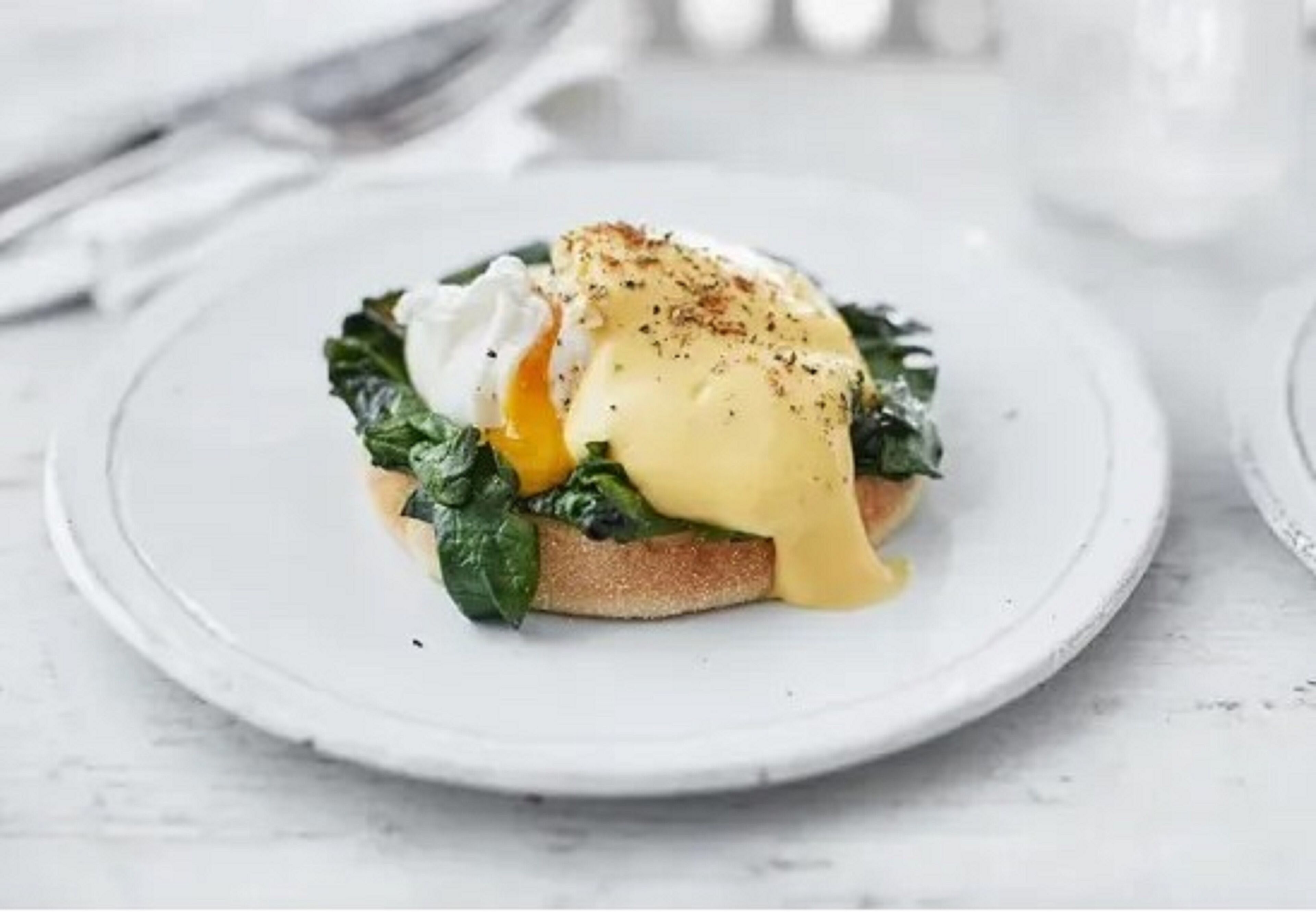 Een bord met gepocheerde ei, spinazie en hollandaisesaus op toast.