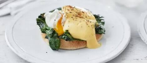 Een bord met gepocheerde ei, spinazie en hollandaisesaus op toast.