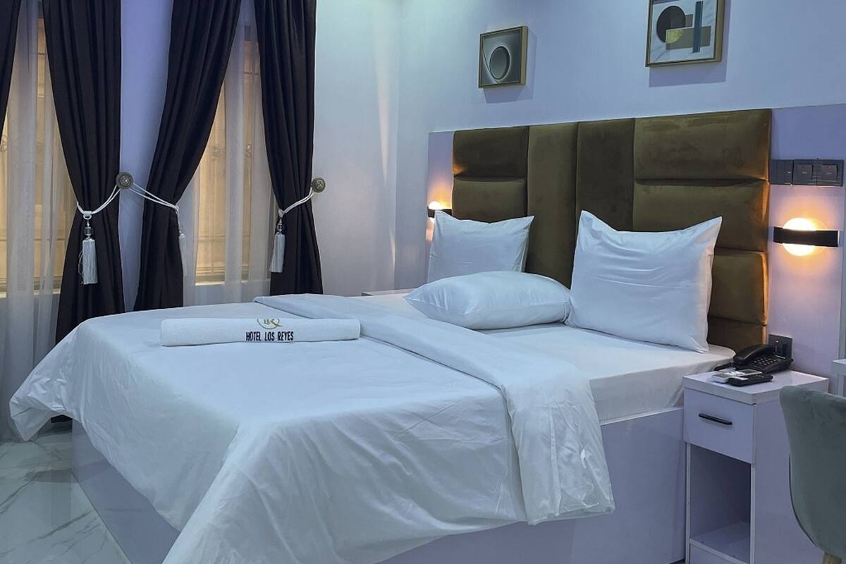 Een hotelkamer met een groot bed, twee nachtkastjes, een lamp en een aan de muur bevestigd telefoon.