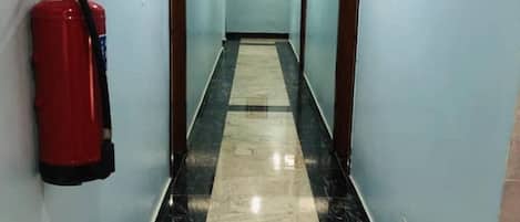 Un pasillo con un extintor en la pared, un cuadro enmarcado y una puerta al final.