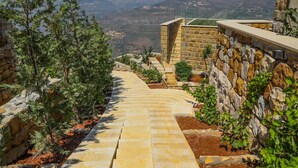 A stone pathway leading uphill with a view of distant mountains and a stone building with a glass balcony. - âl sindiana (Kfar Qatra)