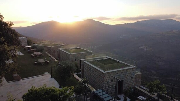 A row of buildings with flat roofs, likely part of a resort or hotel, set against a mountainous backdrop with the sun low on the horizon. - âl sindiana (Kfar Qatra)