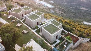 A cluster of stone buildings with flat roofs, surrounded by a landscaped garden and a mountainous backdrop. - âl sindiana (Kfar Qatra)