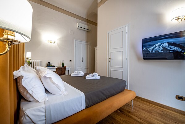 Un dormitorio ordenado con cama, televisor montado en la pared y ventana con cortinas.