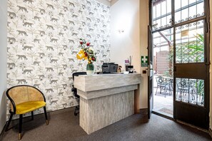 A reception desk with a patterned wallpaper, a vase with flowers, a chair, and a view of the outside through a glass door. - Maison Pitti Florence (Florence)
