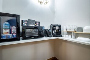 A coffee station with multiple coffee machines, a refrigerator with beverages, and a stack of white cups and plates. - Maison Pitti Florence (Florence)