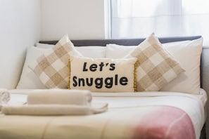 Ein Bett mit einem Kopfkissen mit dem Aufdruck 'Let's Snuggle' und einem darauf liegenden zusammengerollten Handtuch.