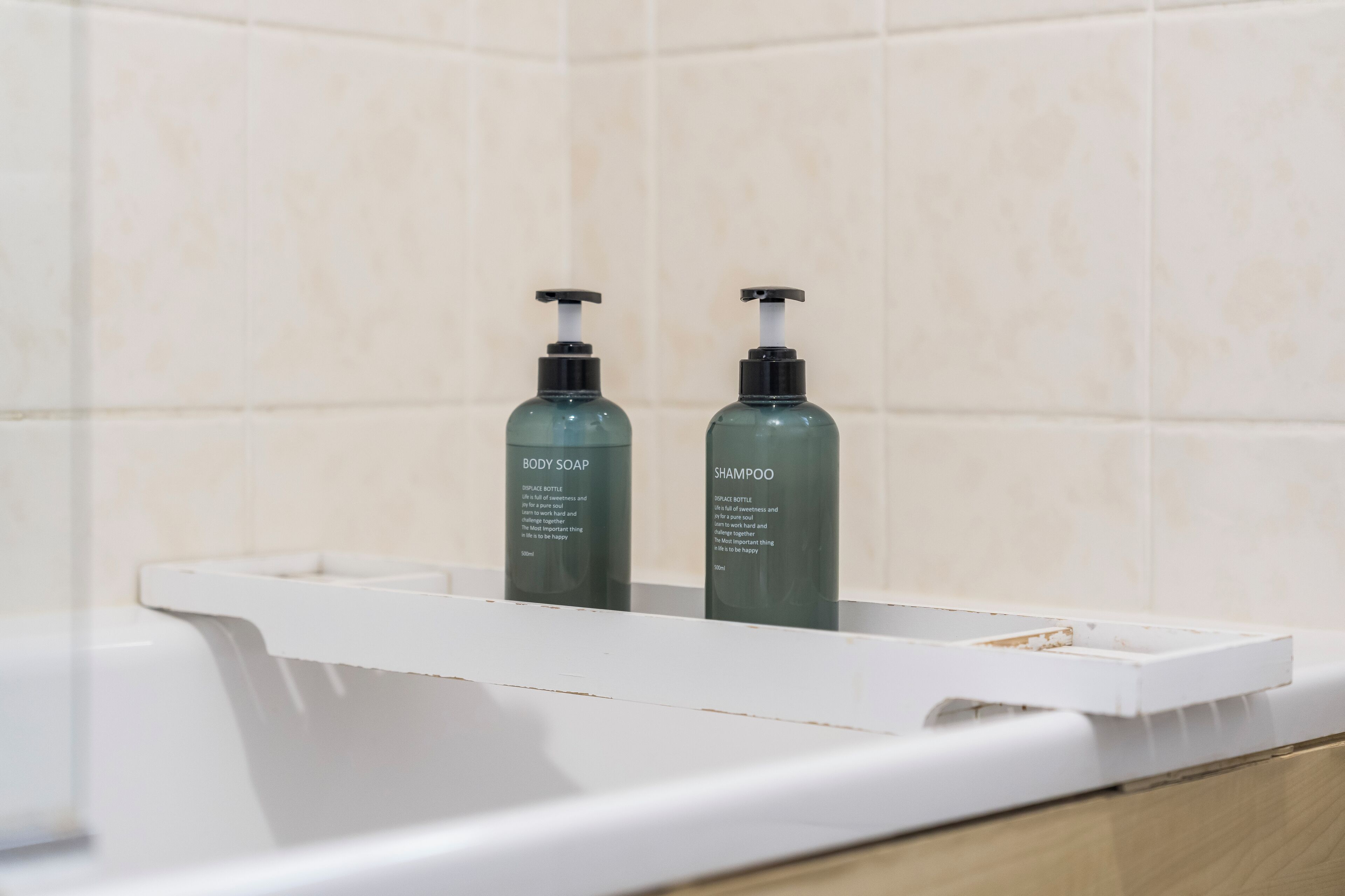 A bathroom with a white countertop, two bottles of body soap and shampoo, and a white sink.