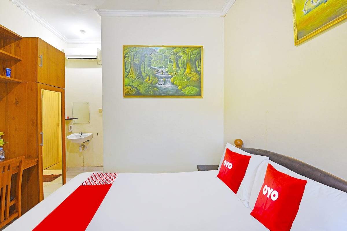 Een hotelkamer met een bed, een houten kast, een wastafel en een schilderij van een boslandschap.