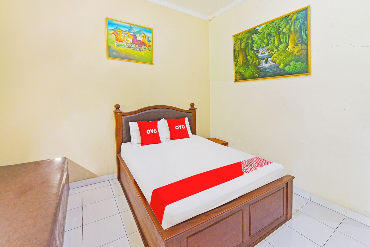 A bedroom with a wooden bed, two paintings on the walls, and a red and white bedspread.