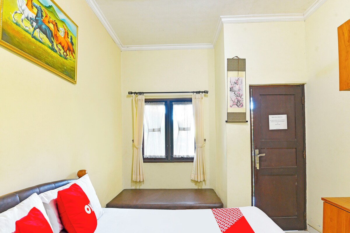 A hotel room with a bed, a window with curtains, a door, and a painting on the wall.