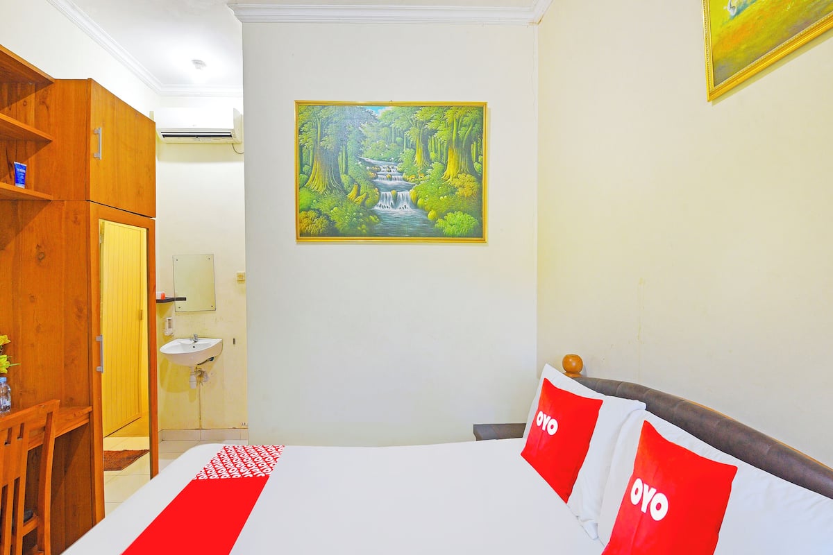 Een hotelkamer met een bed, een houten kledingkast, een boslandschap op een schilderij en een badkamer op de achtergrond.