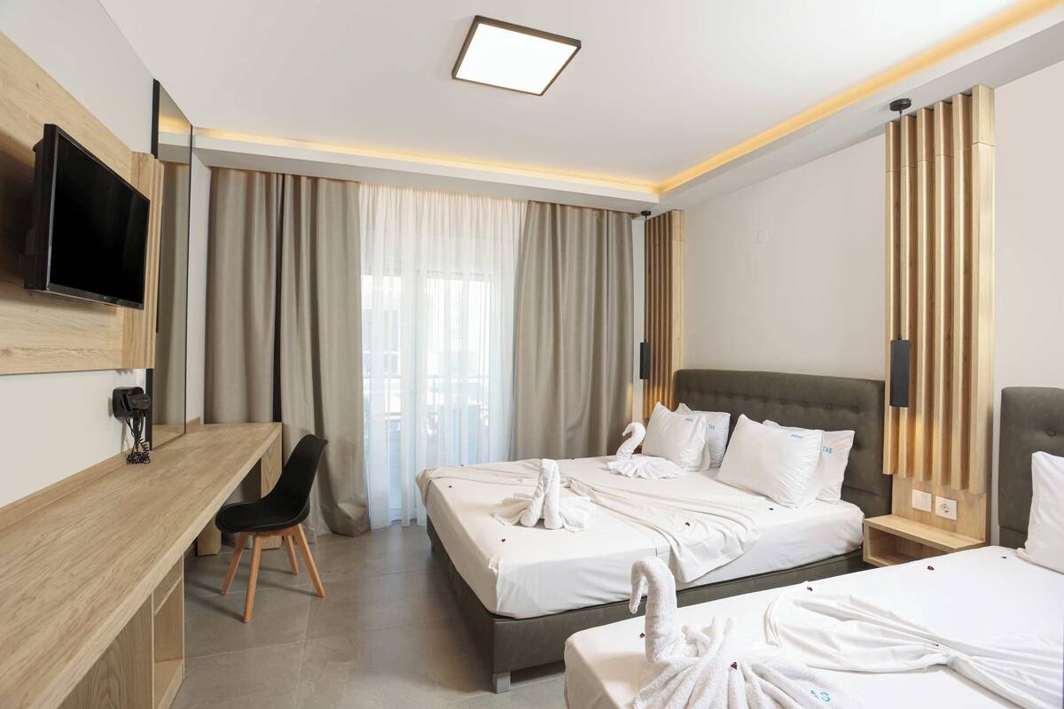 A hotel room with a bed, a desk, a chair, a TV, and a window with curtains.