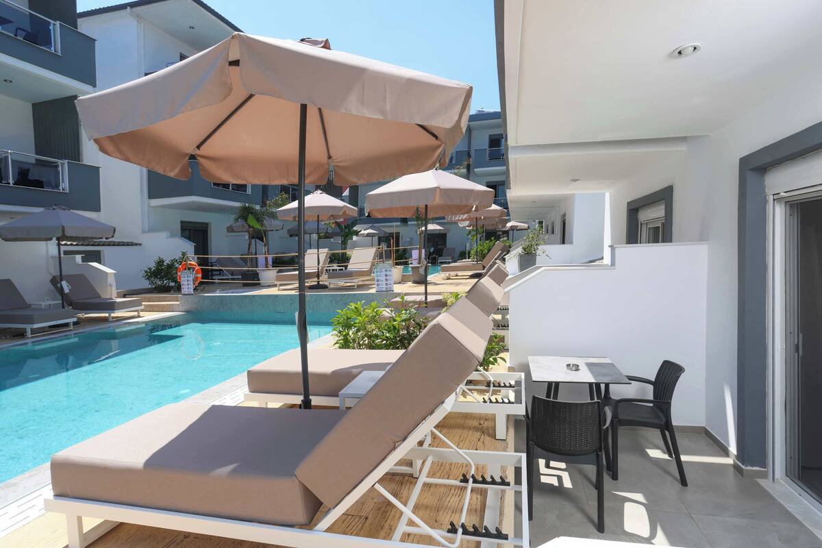 A poolside area with lounge chairs, umbrellas, and a table with chairs.
