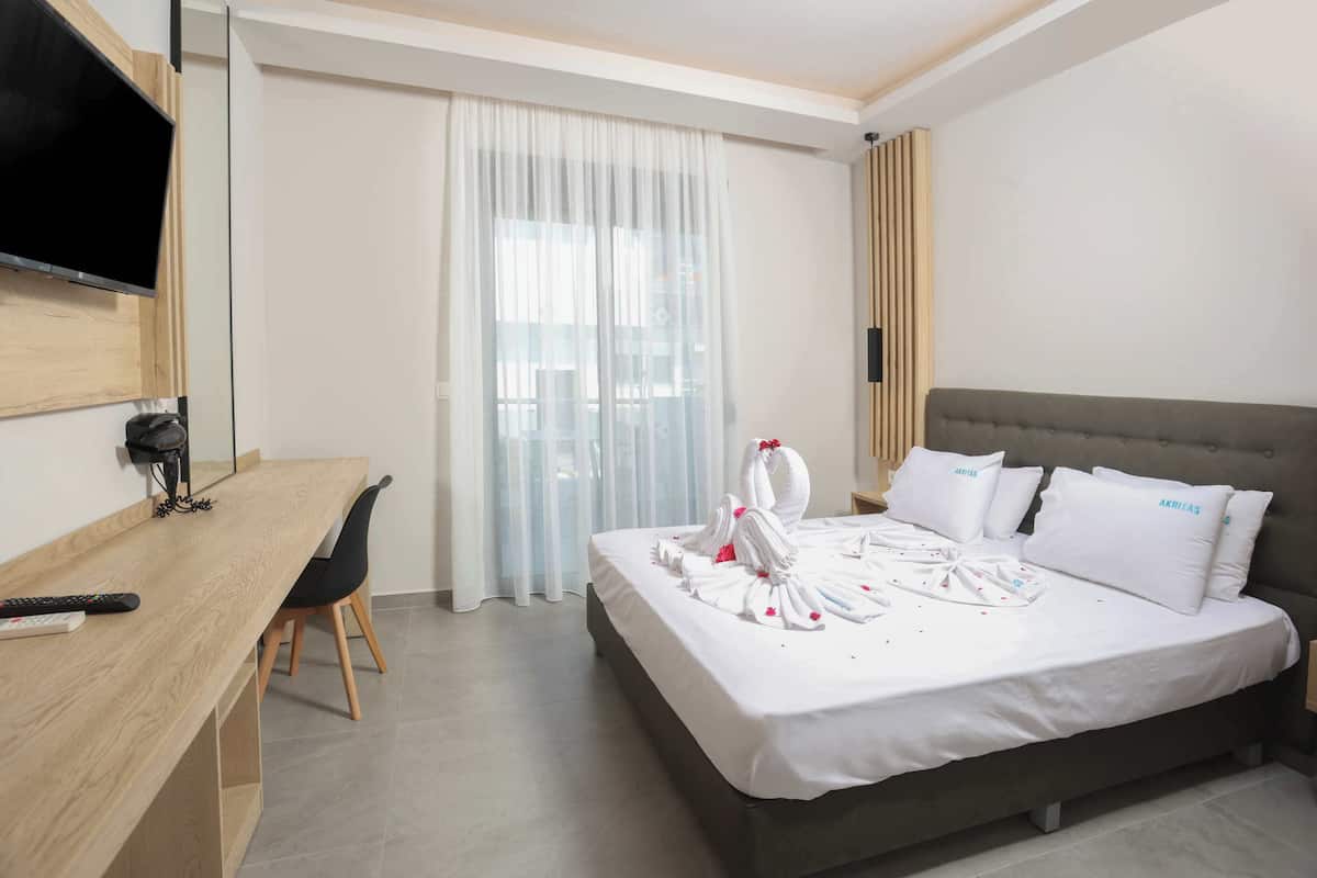 A hotel room with a bed, a desk, a TV, and a window with curtains.