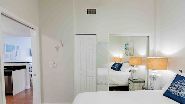 Une chambre à coucher avec un lit, des lampes de chevet, un miroir, une porte et une petite table avec une lampe.