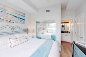 A bedroom with a bed, bedside tables, a mirror, and a view of the kitchen.