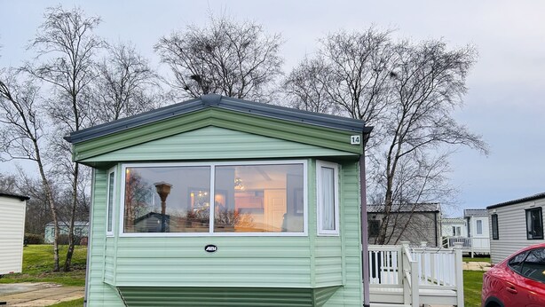A small, single-story mobile home with a green exterior and a white porch. - Charming Countryside Static Van With Entertainment (Wigton)