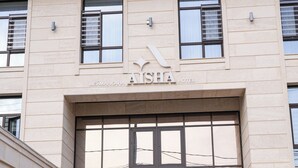 A hotel entrance with a large glass door, a name sign above, and a metal gate. - Aisha Hotel (Bishkek)