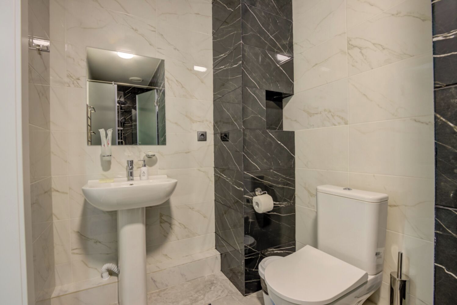 A bathroom with a white sink, a toilet, and marble walls.