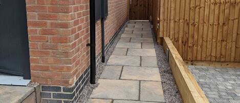 A narrow stone pathway leading to a wooden gate, flanked by a brick wall and a wooden fence.