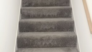 Una escalera con peldaños oscuros cubiertos de alfombra que suben.