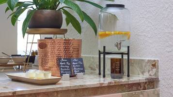A kitchen counter with a potted plant, a copper pot, a glass jar, and a chalkboard menu listing beverages.