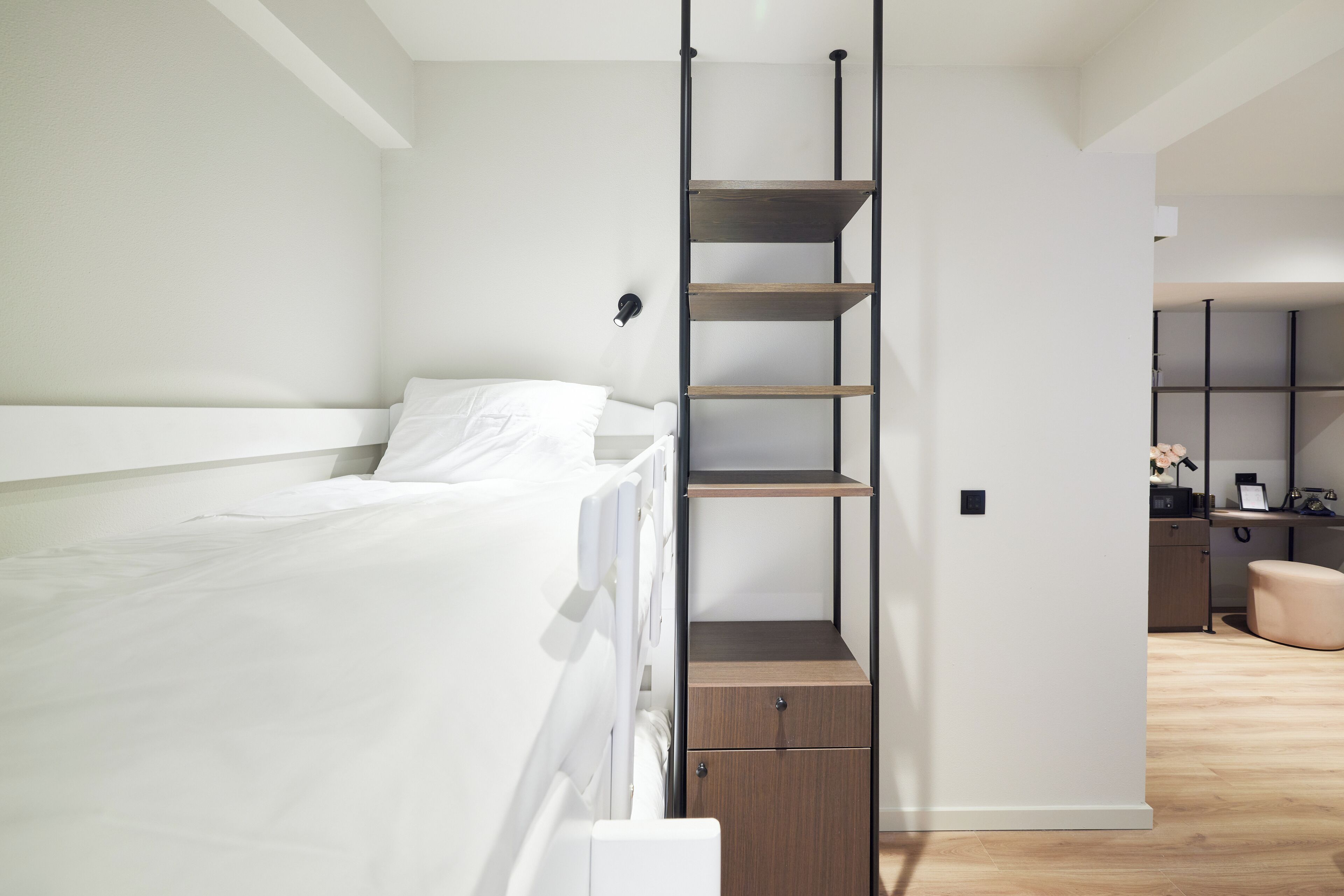 Quarto moderno com beliche, escada de madeira, um pequeno armário e uma escrivaninha com prateleiras ao fundo.