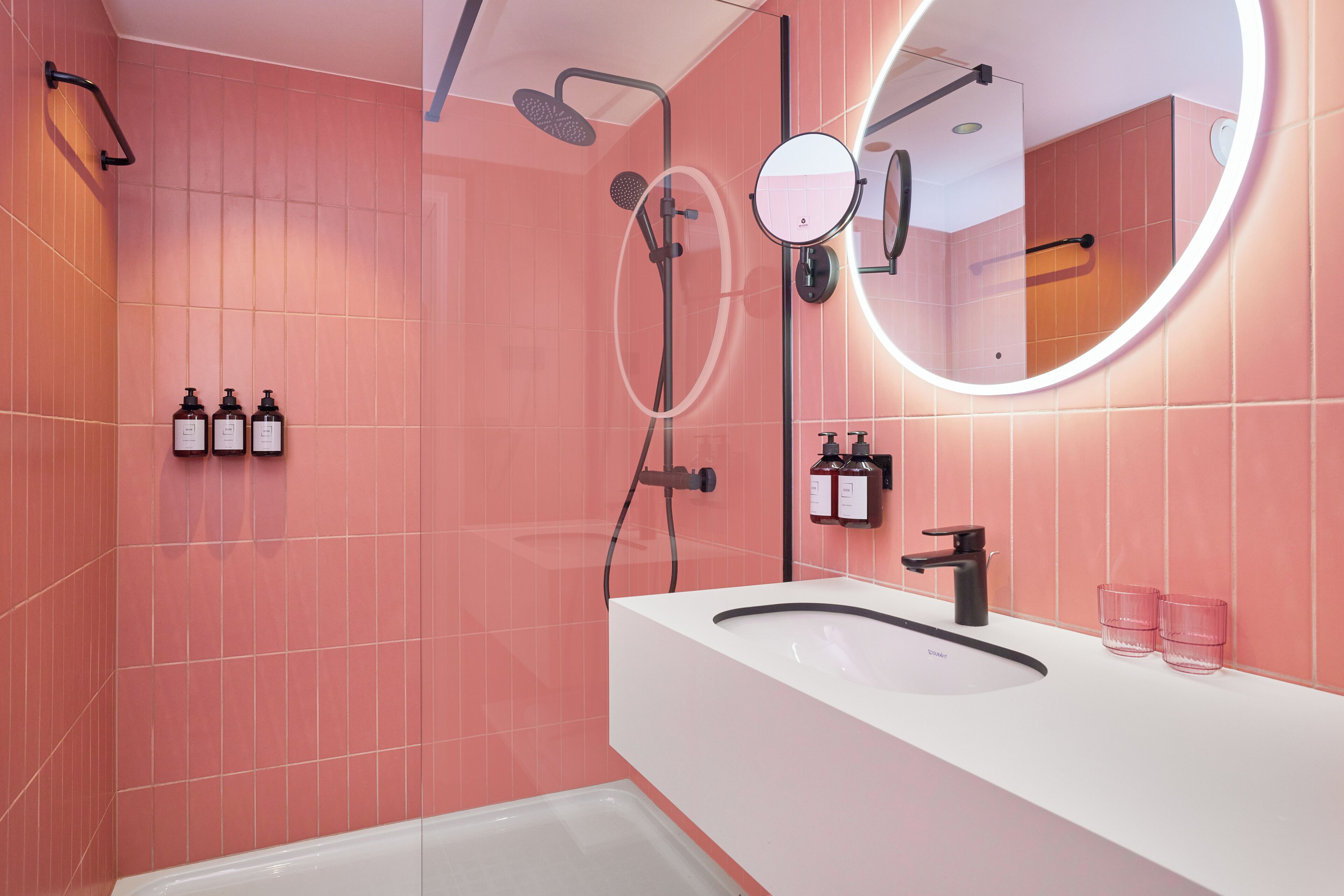 A modern bathroom with a white sink, a round mirror, and a handheld showerhead.