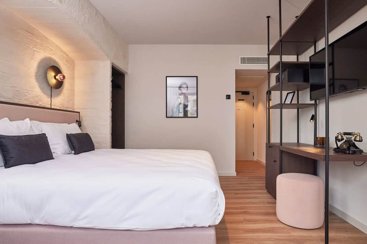 A modern bedroom with a large bed, a wall-mounted light fixture, a framed picture, and built-in shelving with a vintage radio.