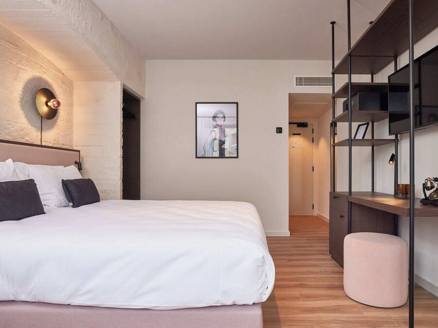 A modern bedroom with a large bed, a wall-mounted light fixture, a framed picture, and built-in shelving with a vintage radio.
