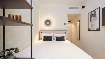 A modern hotel room with a large bed, a desk with a vintage telephone, a wall-mounted light, and a framed picture.