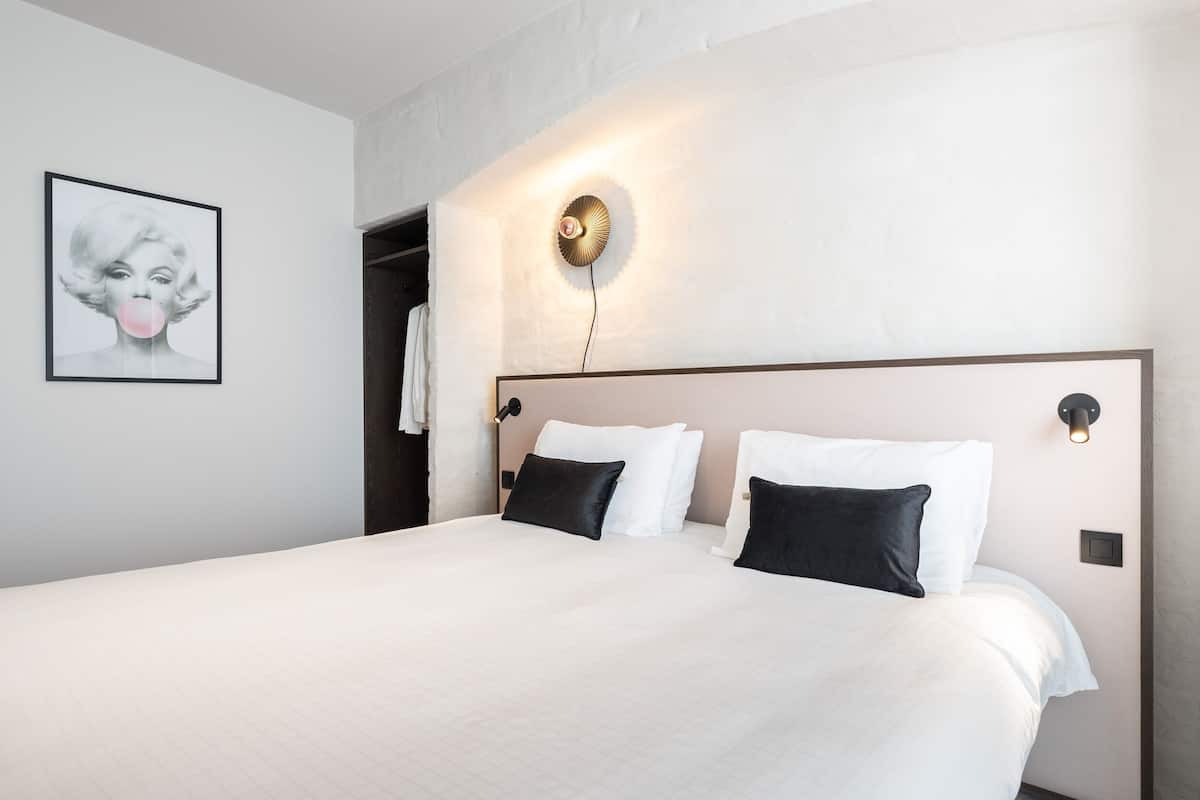 A hotel room with a large bed, a wall-mounted light fixture, and a framed picture on the wall.