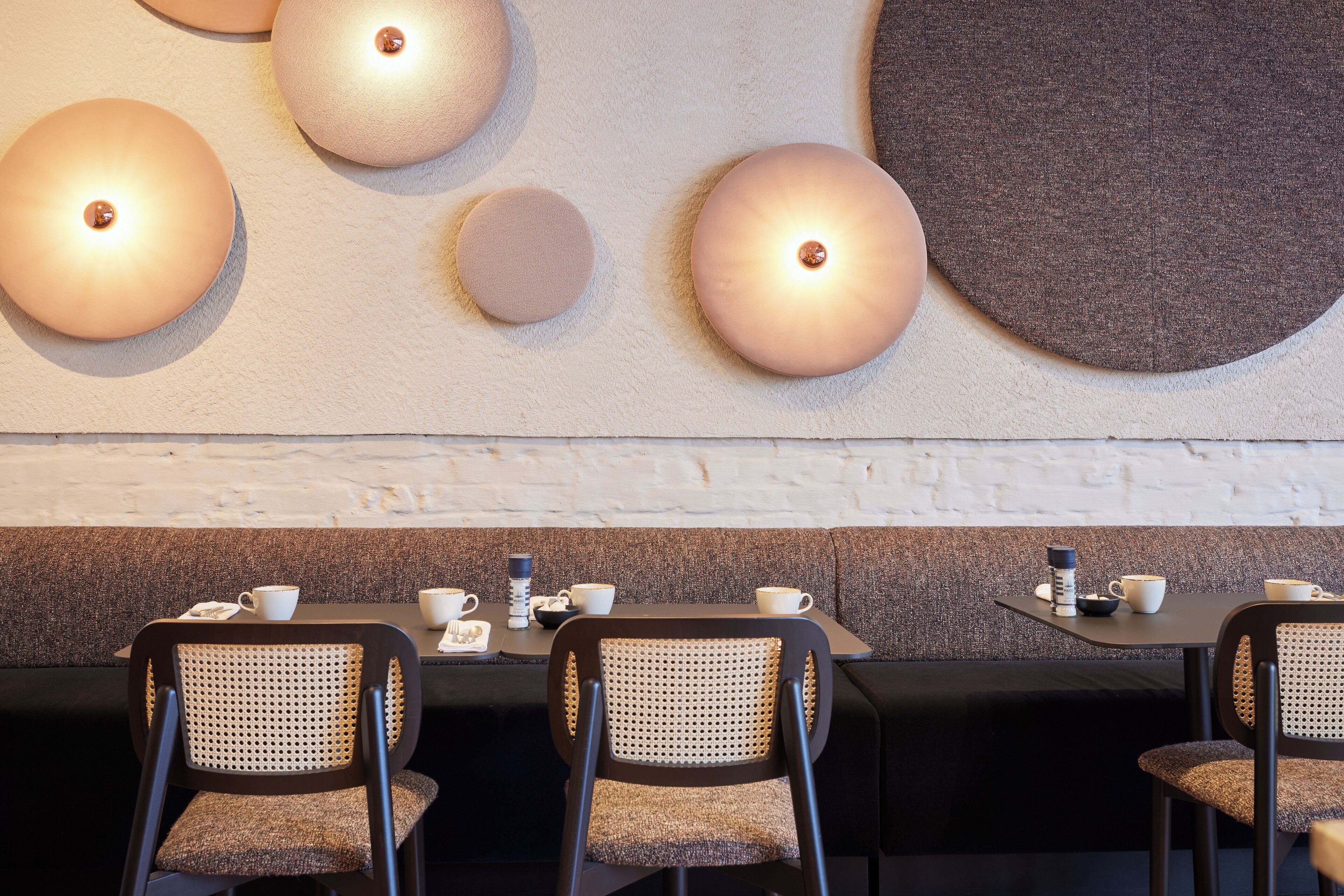 Un comedor moderno con apliques redondos, asientos tapizados en negro y gris, y una pared de ladrillo blanco.