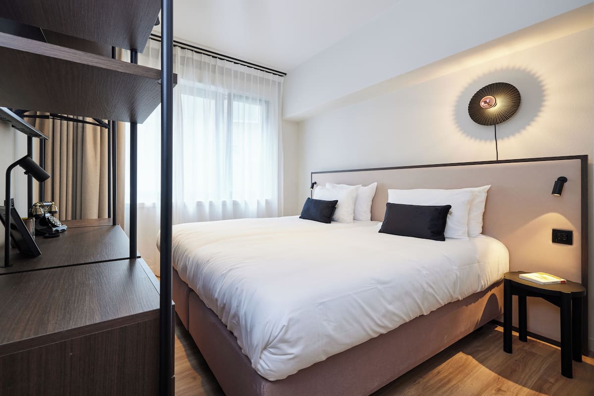 A modern hotel room with a large bed, a bedside table, a lamp, and a wall-mounted light fixture.