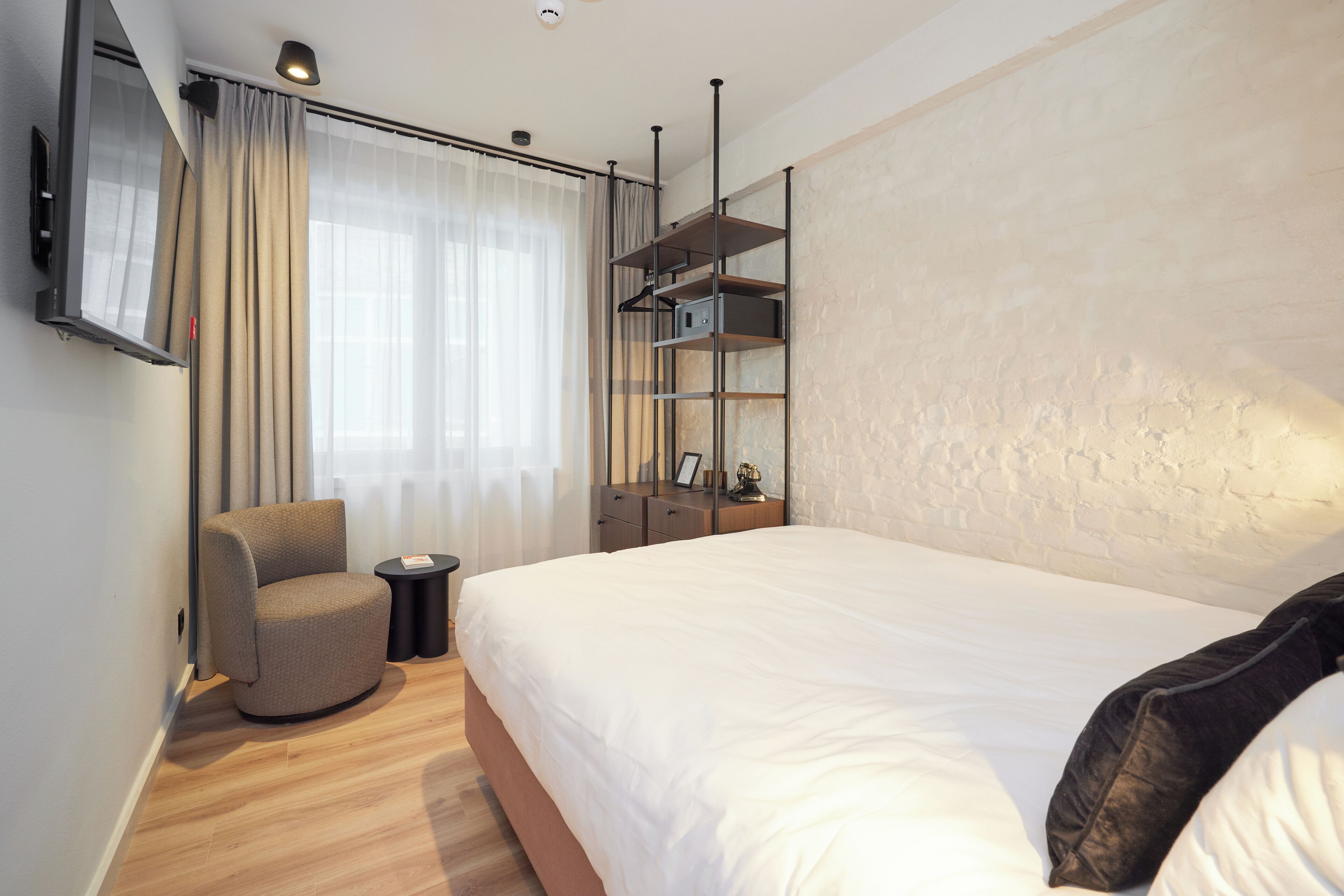 Une chambre d’hôtel moderne avec un grand lit, un coin salon comprenant un fauteuil et une petite table, ainsi qu’un téléviseur fixé au mur.