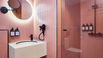 A bathroom with a white sink, a round mirror with a light, and three bottles of toiletries on the wall.