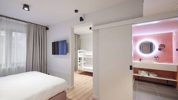 Une chambre d’hôtel moderne, avec un lit, une salle de bain dotée d’un meuble-lavabo rose et donnant sur le couloir.